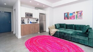 Un soggiorno moderno con un divano verde, un angolo cottura e un tappeto rosa acceso.