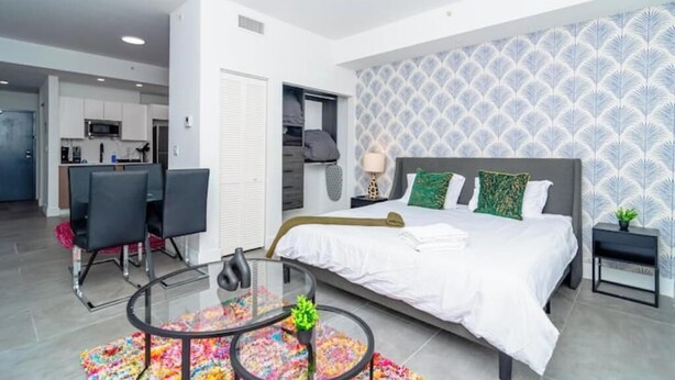 Una camera da letto moderna con un letto grande, un tavolino in vetro e vista sull'area cucina.