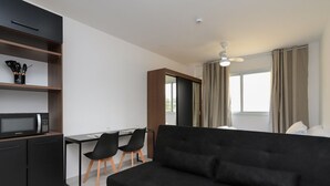 Ein modernes Hotelzimmer mit einer schwarzen Couch, einem Schreibtisch mit zwei Stühlen, einer Mikrowelle und einem Kleiderschrank.