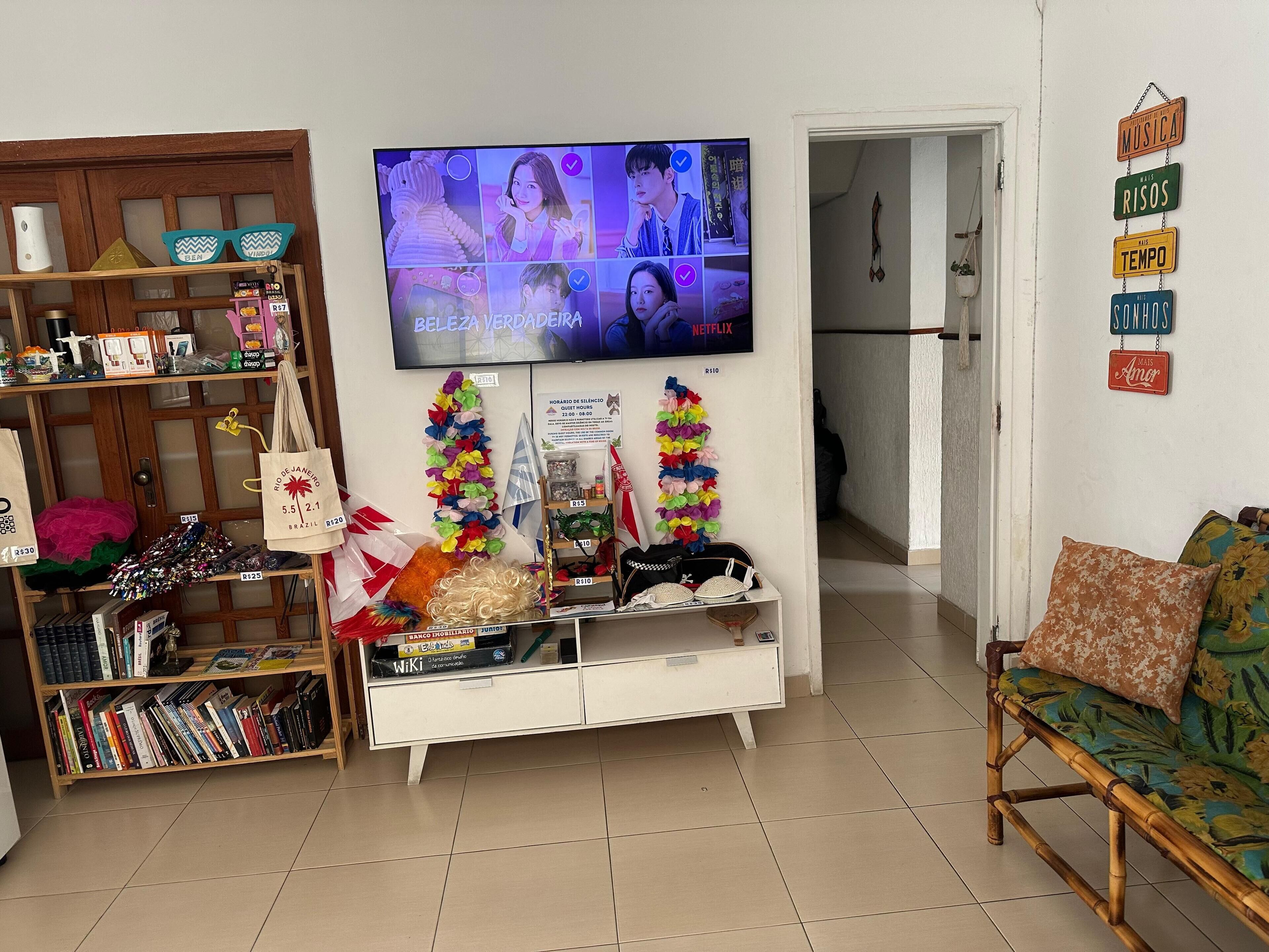 A living room with a television displaying a video call, a bookshelf, a white cabinet, and a sofa with a floral cushion.