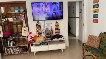 A living room with a television displaying a video call, a bookshelf, a white cabinet, and a sofa with a floral cushion.