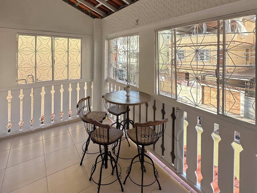 A room with a balcony, a round table with four chairs, and large windows with decorative metal grilles.