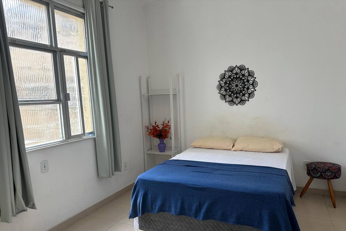 Ein Schlafzimmer mit einem Bett, einem Fenster, einer Wanddekoration und einem kleinen Hocker.