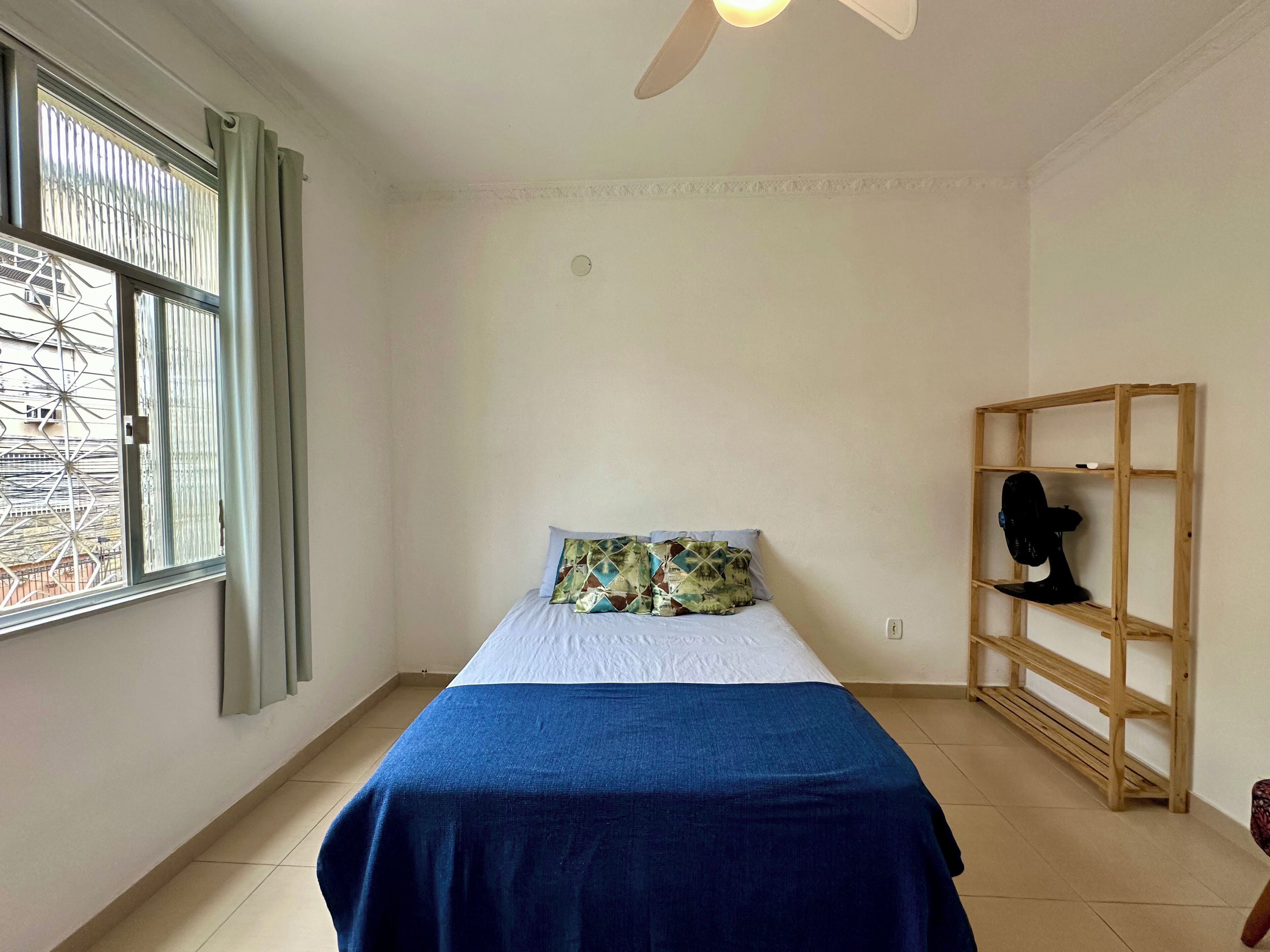 Ein Schlafzimmer mit einem Bett, einem Fenster mit Vorhängen, einem Deckenventilator und einem Holzboden.