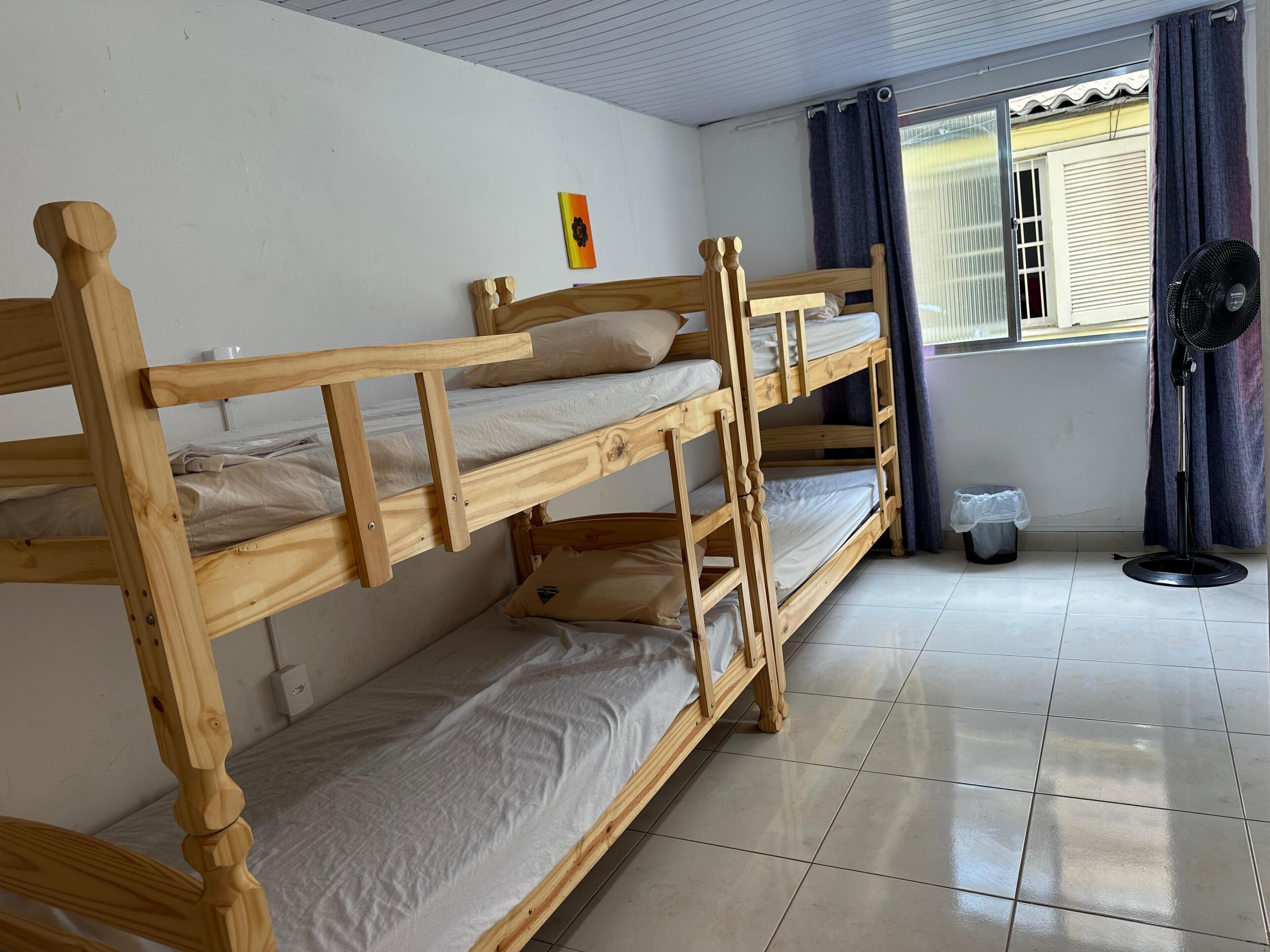 A bunk bed room with a window, a fan, and a small trash bin.