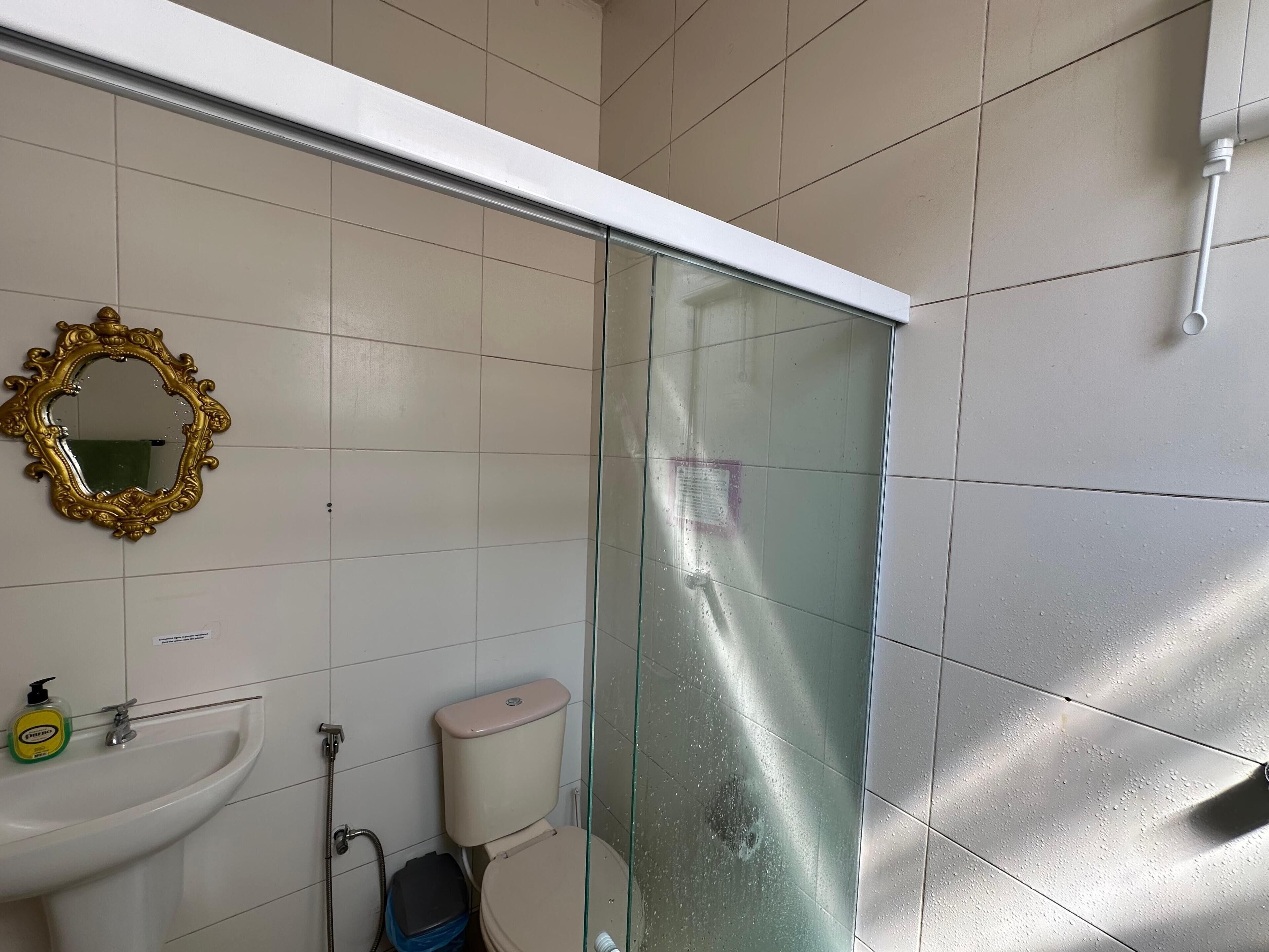 A bathroom with a white sink, a toilet, a glass shower enclosure, and a gold-framed mirror.
