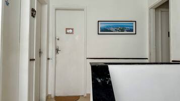 Um corredor com uma porta branca, um quadro de uma paisagem costeira e um banco de mármore preto.