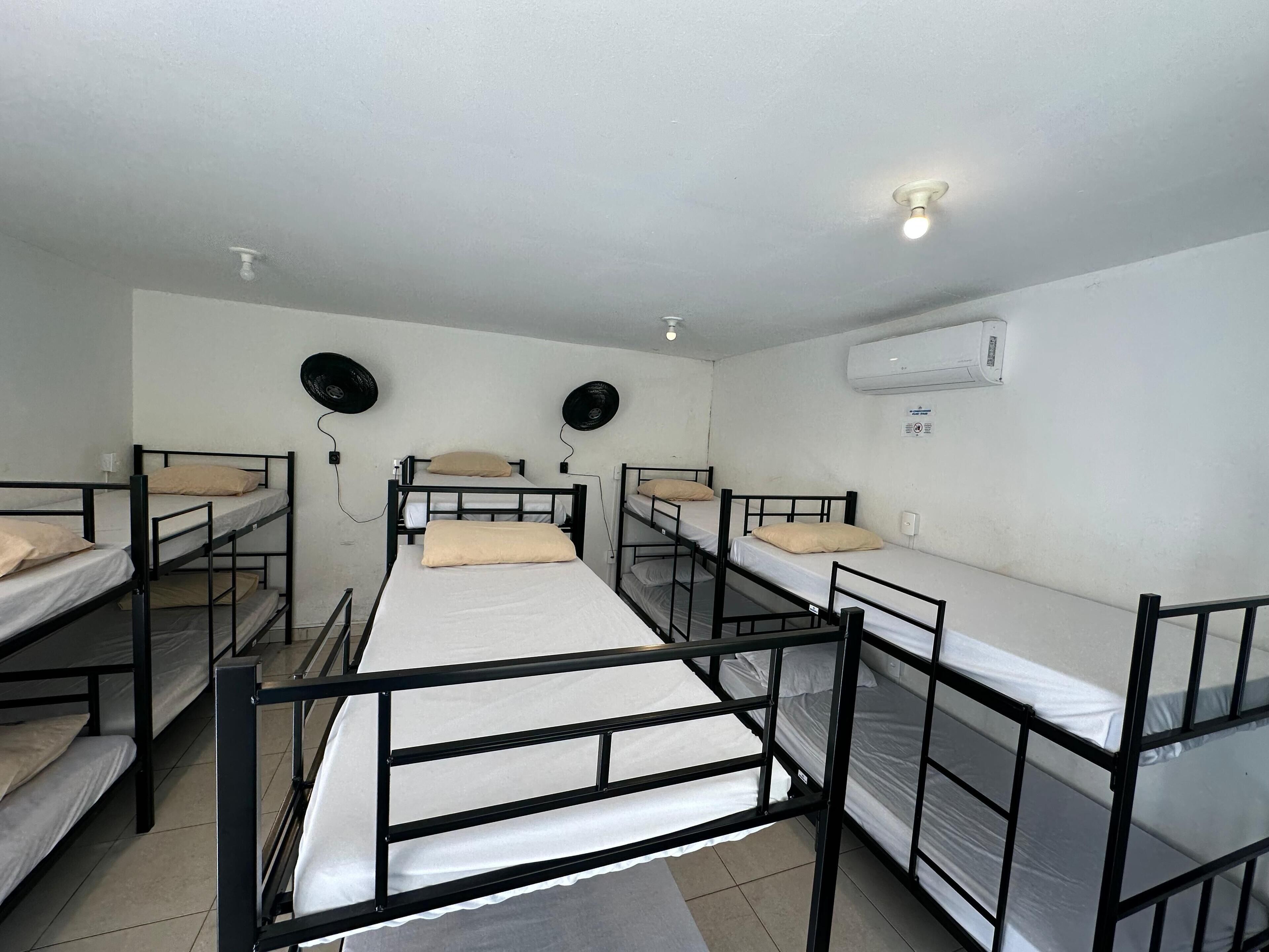 A dormitory room with bunk beds, an air conditioning unit, and a ceiling light.