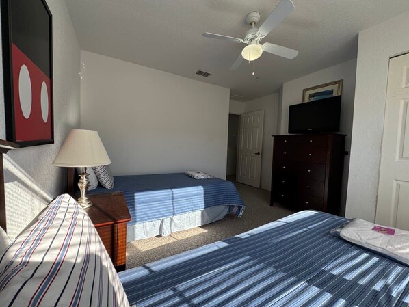 A bedroom with two beds, a ceiling fan, a dresser, and a television.