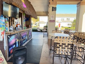 An outdoor bar area with a thatched roof, karaoke setup, and outdoor seating.