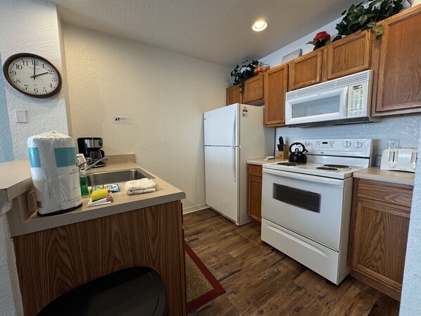 A compact kitchen with wooden cabinets, a white refrigerator, a microwave, a stove, and a sink.