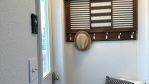 Un couloir avec un banc en bois, une étagère murale ornée de plantes en pot, un chapeau et un coussin à rayures.