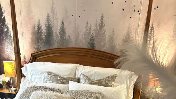 Un lit bien fait, avec une literie blanche et grise, une tête de lit en bois et une table de chevet sur laquelle se trouvent une lampe et une bougie.