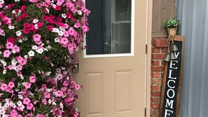 Une porte ornée d’une pancarte « BIENVENUE », un paillasson et une composition florale suspendue.