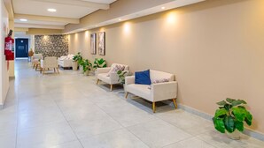 A hallway with a row of white sofas and armchairs, a fire extinguisher, and a potted plant. - Studio 617 - Santana (São Paulo)