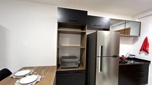 A compact kitchen with a built-in microwave, a refrigerator, and a small countertop with a stove. - Studio 621 - Santana (São Paulo)