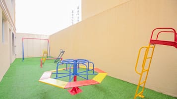 A children's play area with various equipment including a seesaw, a swing set, and a climbing structure.