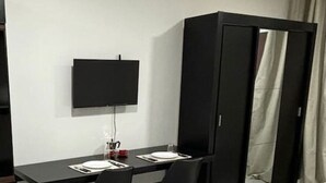 Una habitación de hotel con cama, escritorio con dos sillas, armario y televisión en la pared.