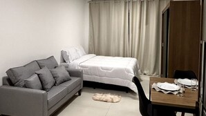 Ein modernes Schlafzimmer mit einem Bett, einem grauen Sofa, einem Esstisch mit Stühlen und einem kleinen Teppich.