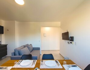 A modern living room with a sofa, a dining table set with plates, cutlery, and glasses.