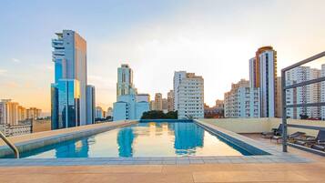Piscina no terraço com vista para a cidade, cercada por edifícios altos.