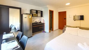 Habitación de hotel con cama, escritorio con silla, kitchenette, televisor y puerta.
