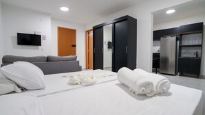 Una habitación de hotel moderna con cama, sofá, televisor, armario y kitchenette.