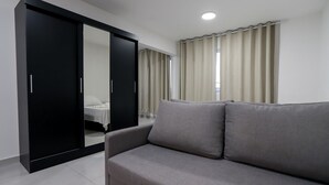 Una habitación moderna con un sofá gris, un armario negro y una cama con ropa de cama blanca.