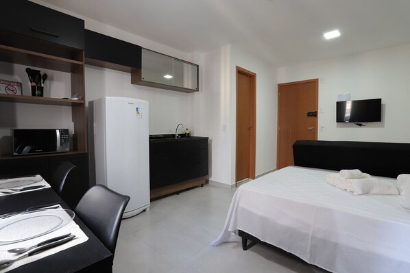 A hotel room with a bed, a desk with a chair, a refrigerator, a microwave, a sink, and a television.
