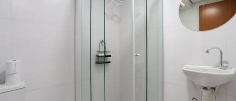 Un baño moderno con ducha de vidrio, lavamanos blanco y un inodoro.