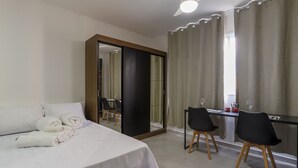 A hotel room with a bed, a desk, two chairs, a mirror, and a window with curtains.