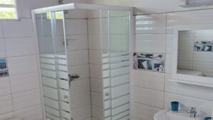 A bathroom with a glass-enclosed shower, a toilet, a sink, and a blue trash bin. - BEAUTIFUL 1ST-FLOOR VILLA APARTMENT (Sainte-Anne)