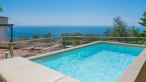 A rectangular swimming pool with a clear blue water, surrounded by a white deck and a metal railing. - AMORE RENTALS - Villa Jacaranda with Pool and Sea View (Praiano)