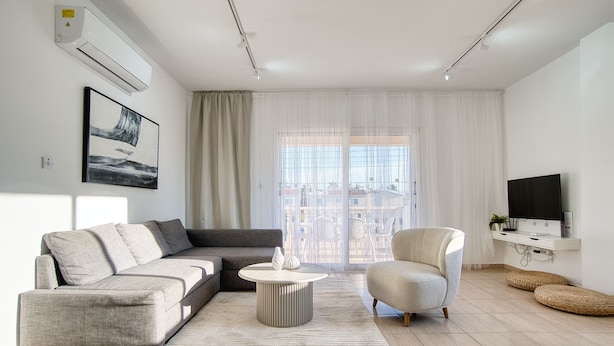 Un salon moderne avec un canapé gris, une table basse ronde, un fauteuil blanc et un téléviseur à écran plat posé sur un meuble blanc.
