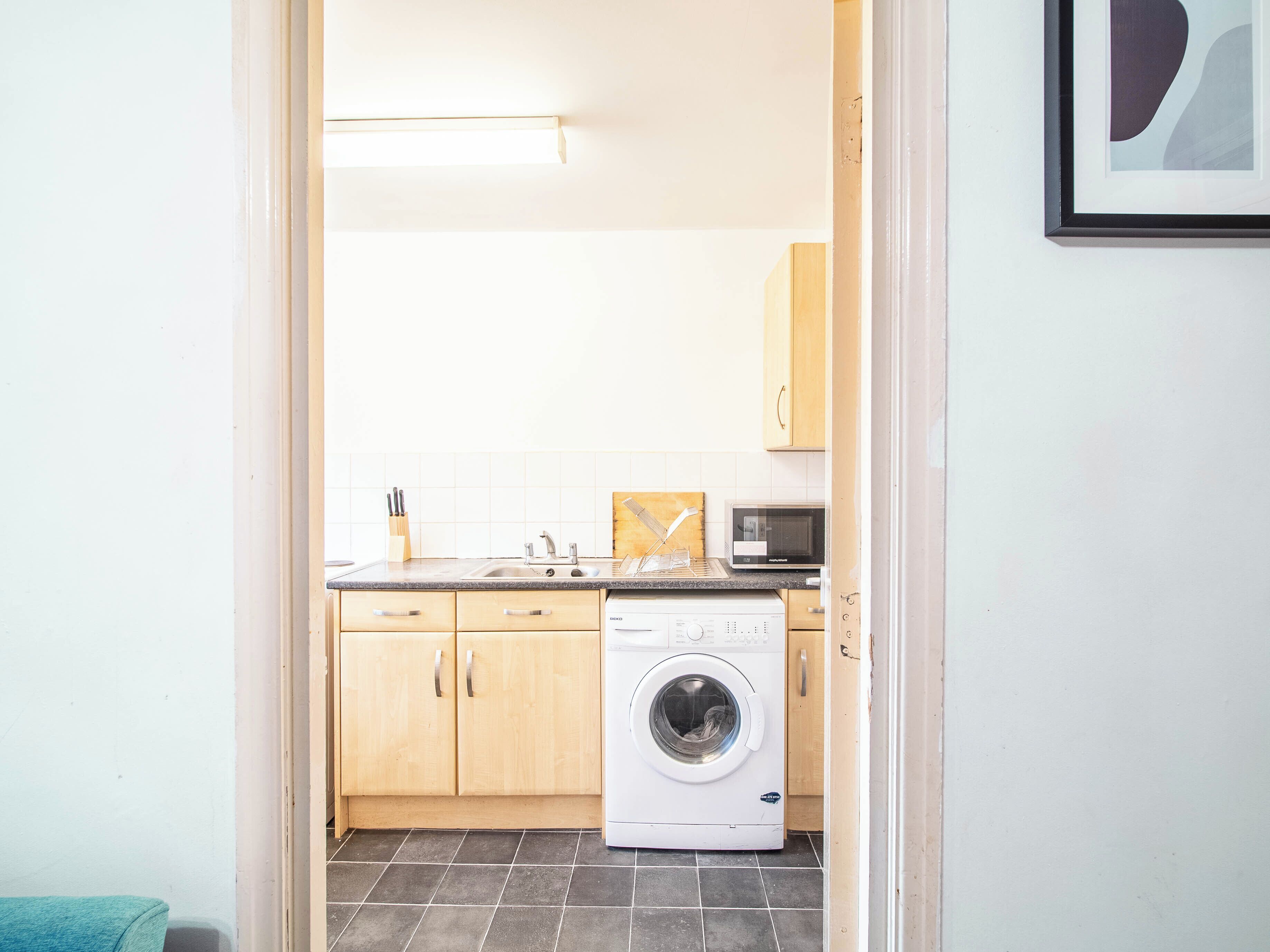 A compact kitchen with a washing machine, a microwave, and wooden cabinets.
