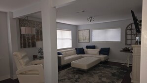Een woonkamer met een hoekbank, een fauteuil, een kamerkleed en een open haard.