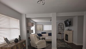 Een woonkamer met een witte bank, een boekenkast, een open haard en een televisie aan de muur.