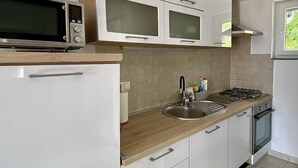 Una cocina moderna con armarios blancos, un fregadero de acero inoxidable, un microondas y una estufa a gas.
