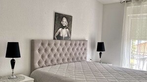 Un dormitorio con cabecera capitonada, colcha acolchada, dos mesitas de noche con lámparas y un cuadro en la pared.