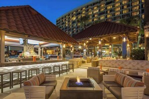 An outdoor lounge area with seating, a fire pit, and a view of a hotel building.