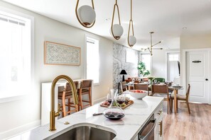 A modern kitchen with a marble countertop, gold faucets, and pendant lighting.