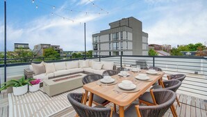 A rooftop terrace with a wooden dining table, chairs, a sofa, and string lights.
