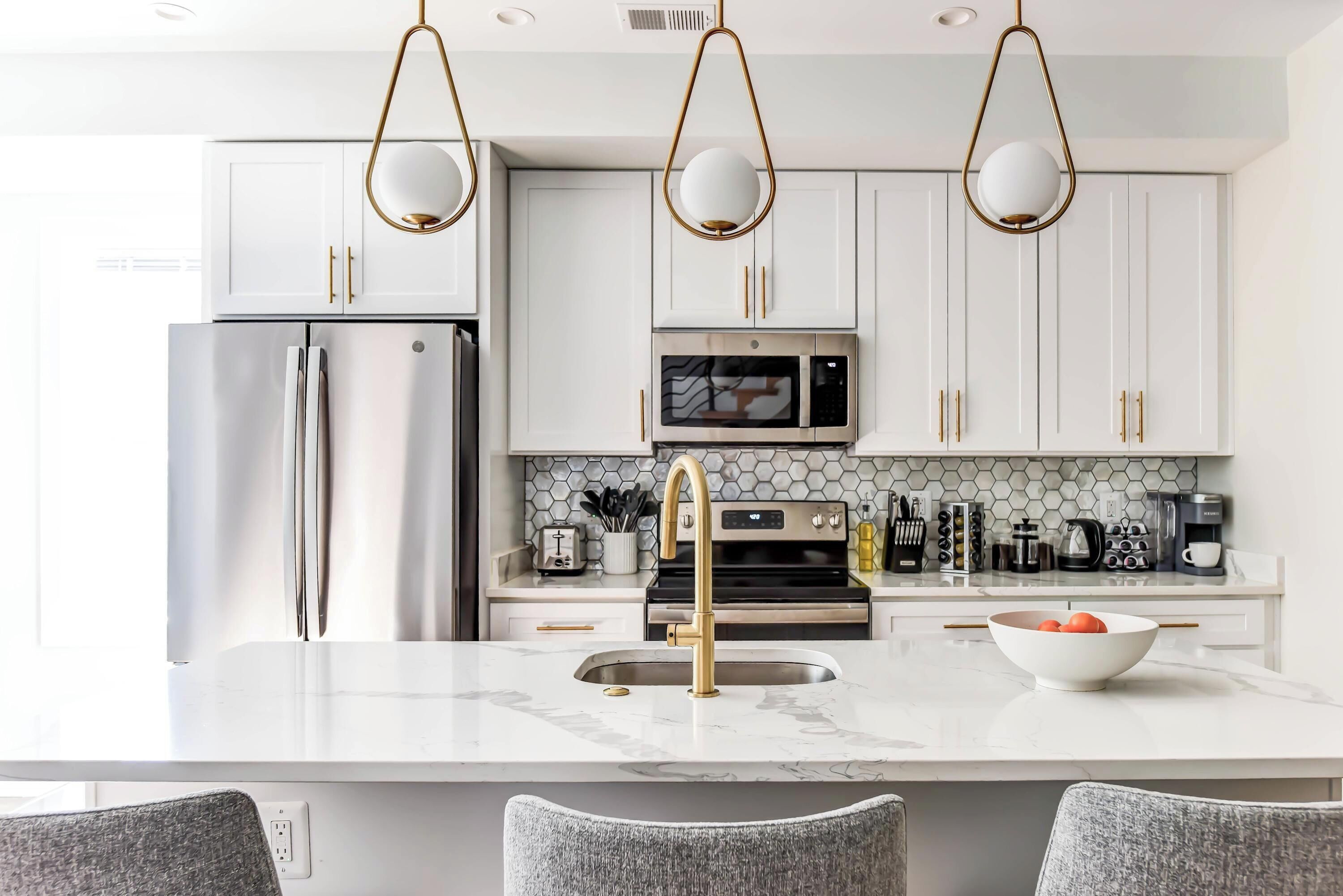 A modern kitchen with white cabinets, stainless steel appliances, and a marble countertop.