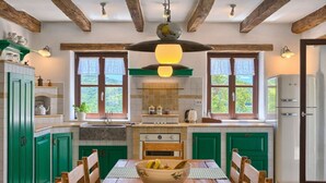 A kitchen with wooden beams, green cabinets, a dining table with chairs, and a refrigerator.
