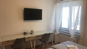 Ein Hotelzimmer mit einem Bett, einem Schreibtisch mit zwei Stühlen, einem Fernseher und einem Fenster mit Vorhängen.