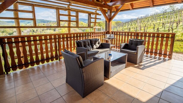 A covered outdoor seating area with wicker furniture and a view of vineyards.
