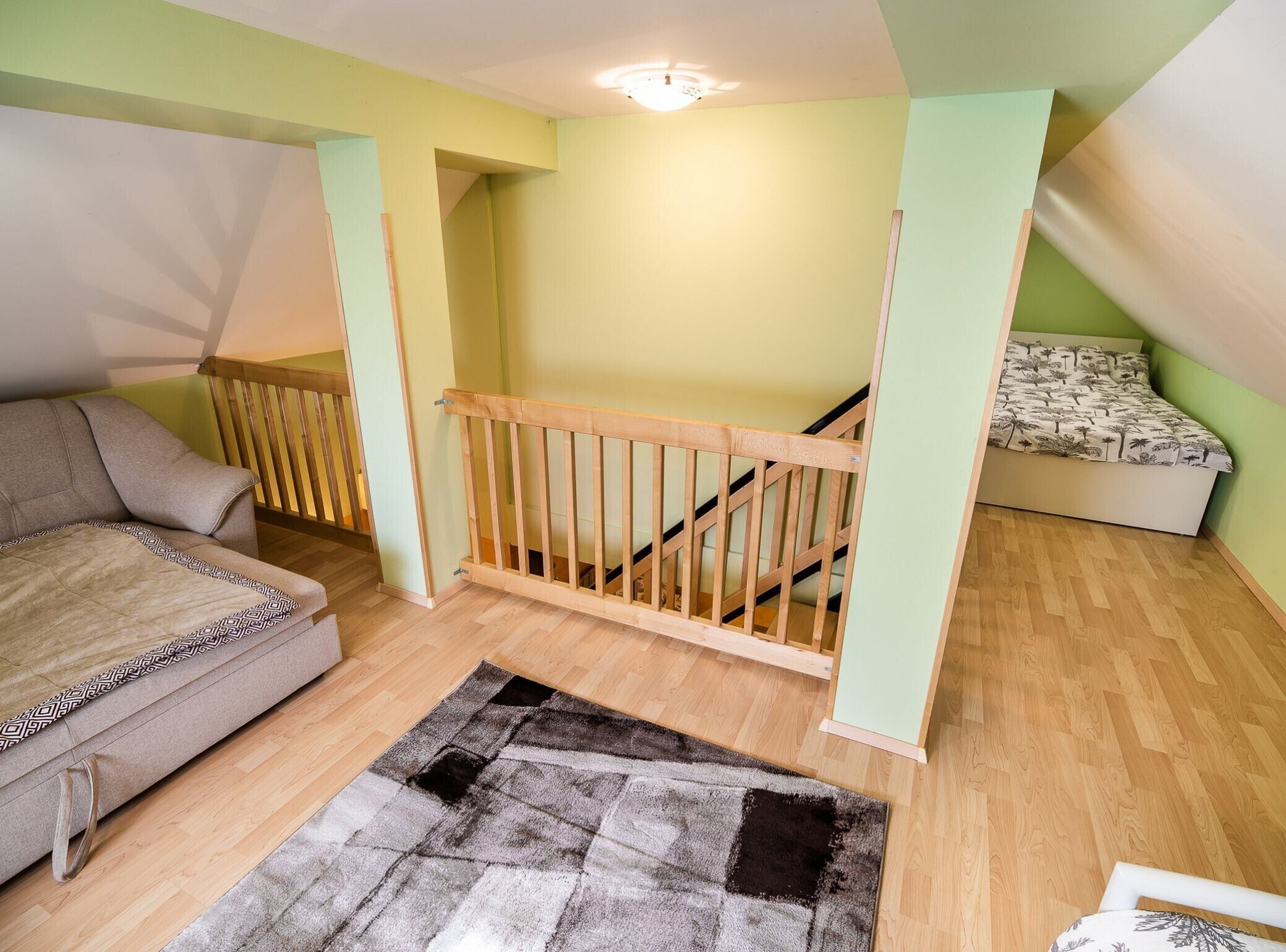 Una habitación con escalera de madera, un sofá, una cama con colcha estampada y un tapete a cuadros.