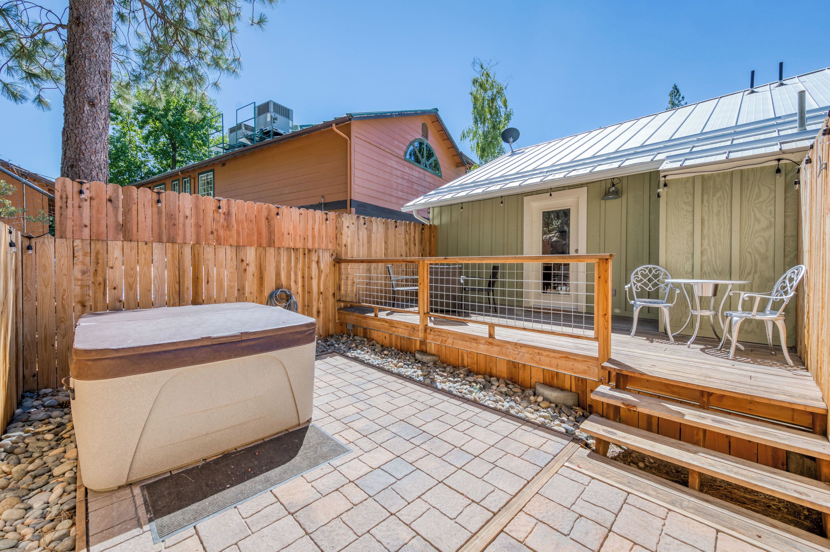 Une terrasse en bois avec un jacuzzi, un patio clos et un bâtiment doté d’un toit en métal.