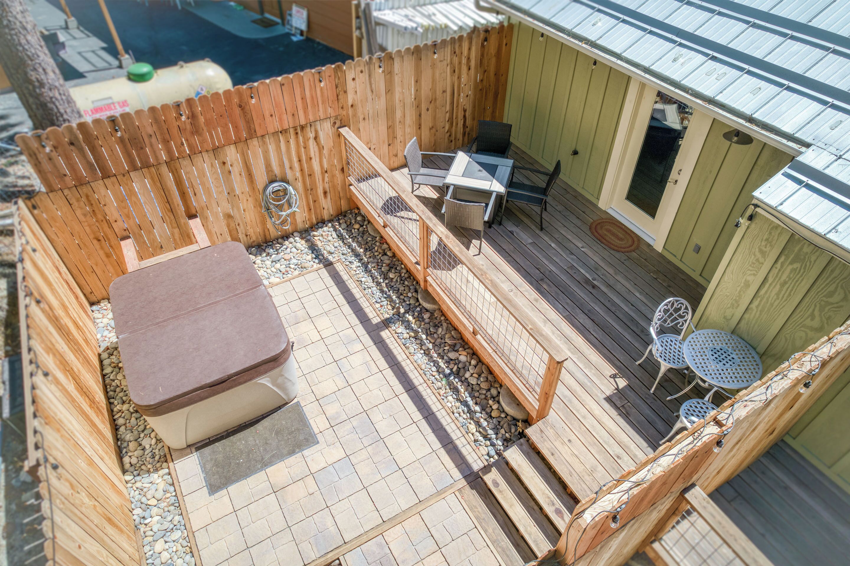 A wooden deck with a hot tub, a table with chairs, and a small garden area with a wooden fence.