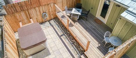 A wooden deck with a hot tub, a table with chairs, and a small garden area with a wooden fence.